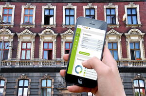 Handy mit GebäudeCheck und im Hintergrund ein Gebäude