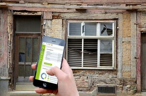 Handy mit GebäudeCheck mit altem Gebäude im Hintergrund