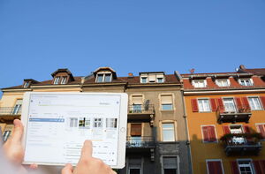 Tablet mit GebäudeCheck App und im Hintergrund Gebäude