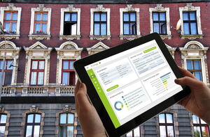 Tablet mit GebäudeCheck Screen und im Hintergrund ein Gebäude