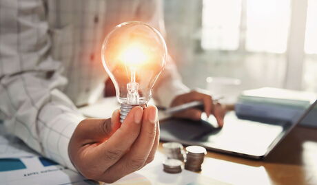 Mann hält Glühbirne in der Hand während er am Laptop arbeitet