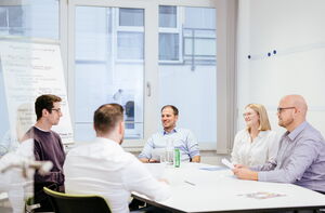 Teammeeting aus 5 Leuten um den Besprechungstisch