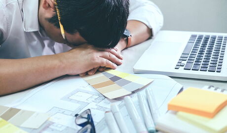 Ein überarbeiteter Architekt der seinen Kopf auf den Tisch legt.