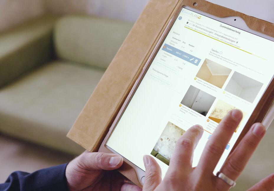 Im Vordergrund Tablet mit der GebäudeCheck App und im Hintergrund eine Couch